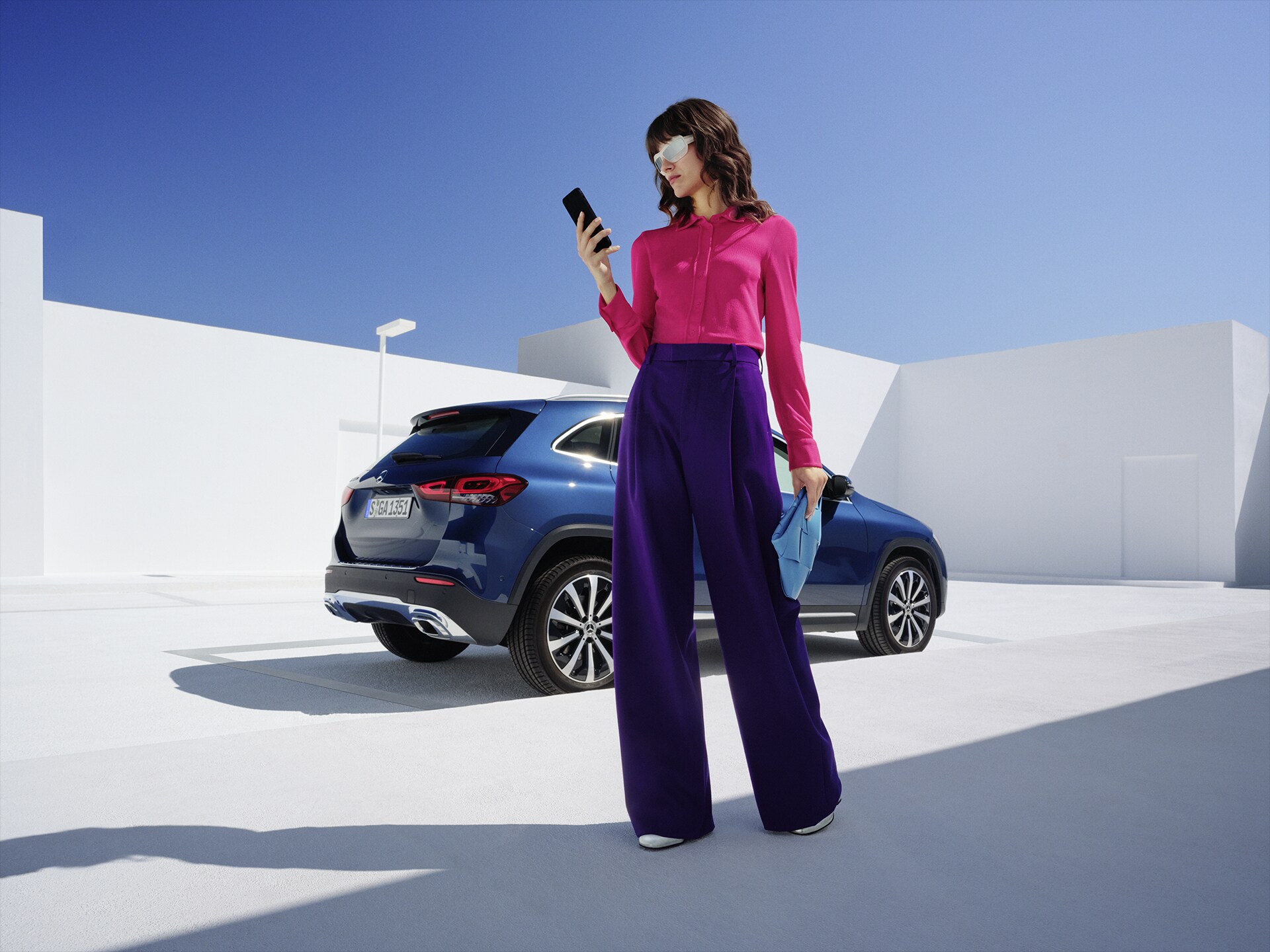 Women stands in front of the Mercedes-Benz GLA and is looking on her phone.