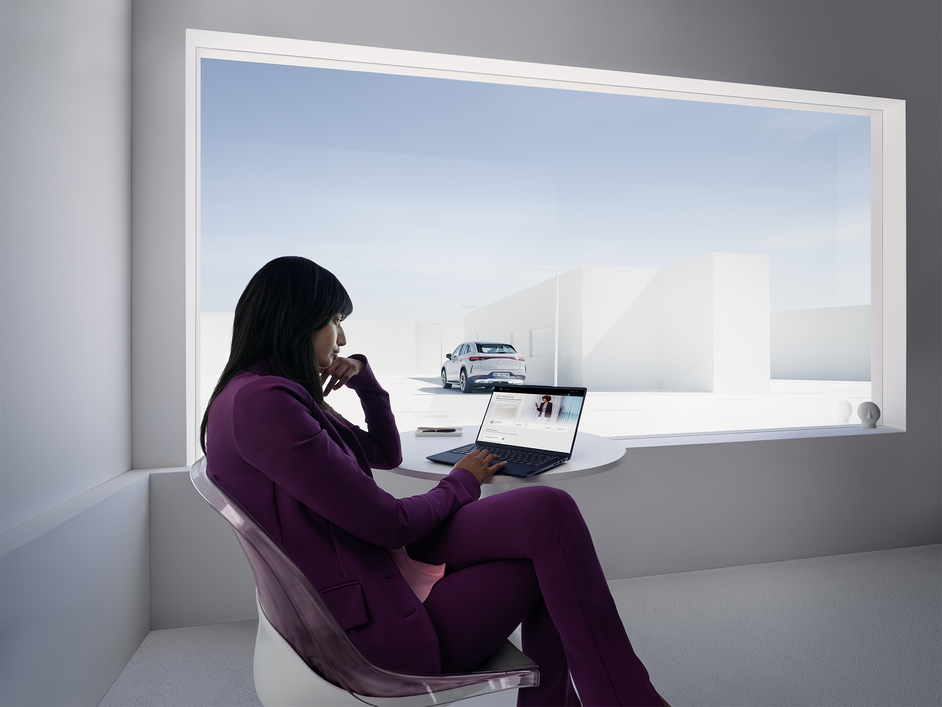 Business Profile Benefits | Mercedes me ID | Mercedes-Benz A woman working at a laptop sits in a white office in front of a large window.