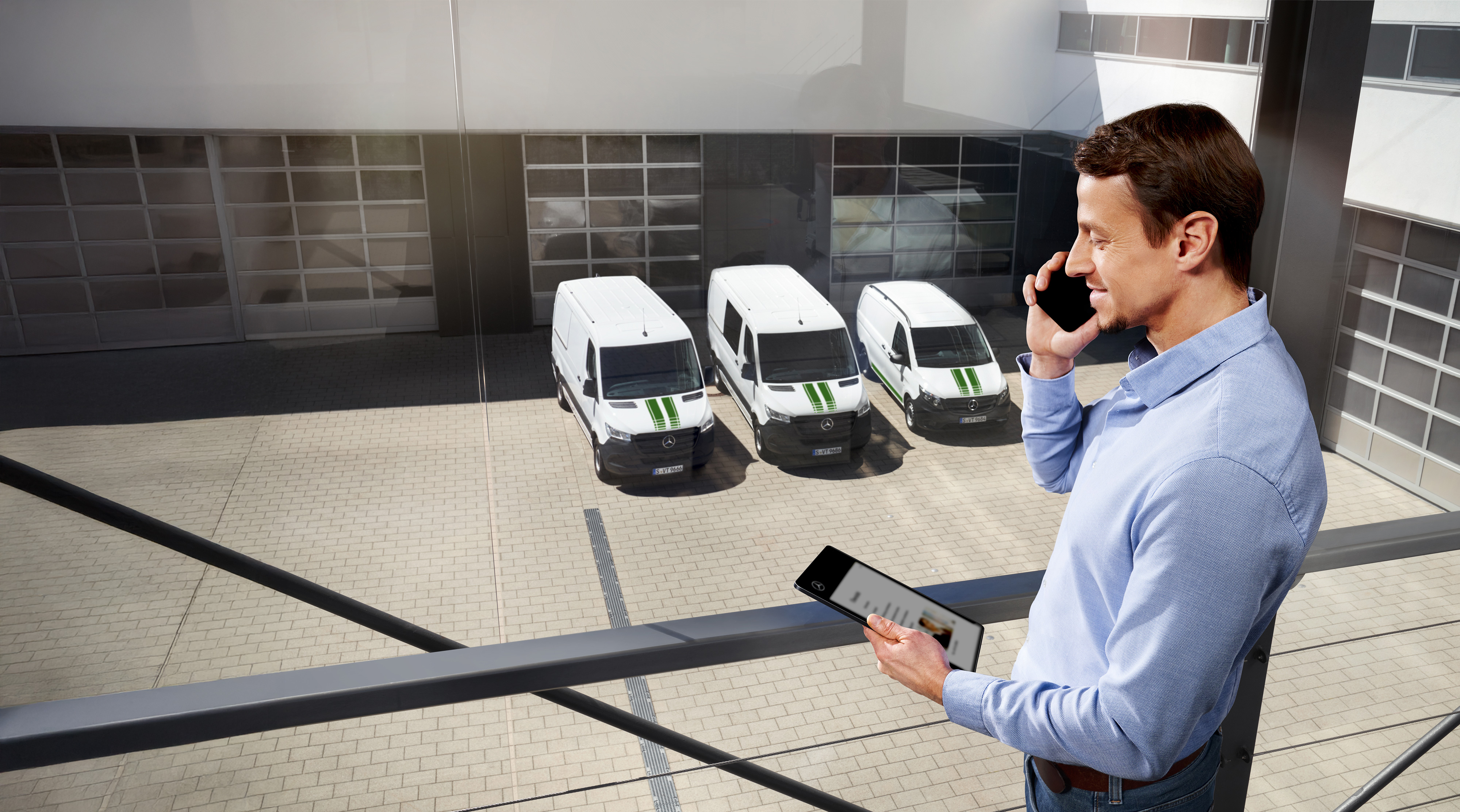 Mercedes-Benz | Vans Care | Roadside Assistance A man talking on a mobile phone in front of a small fleet of white Mercedes-Benz vans in a car park.