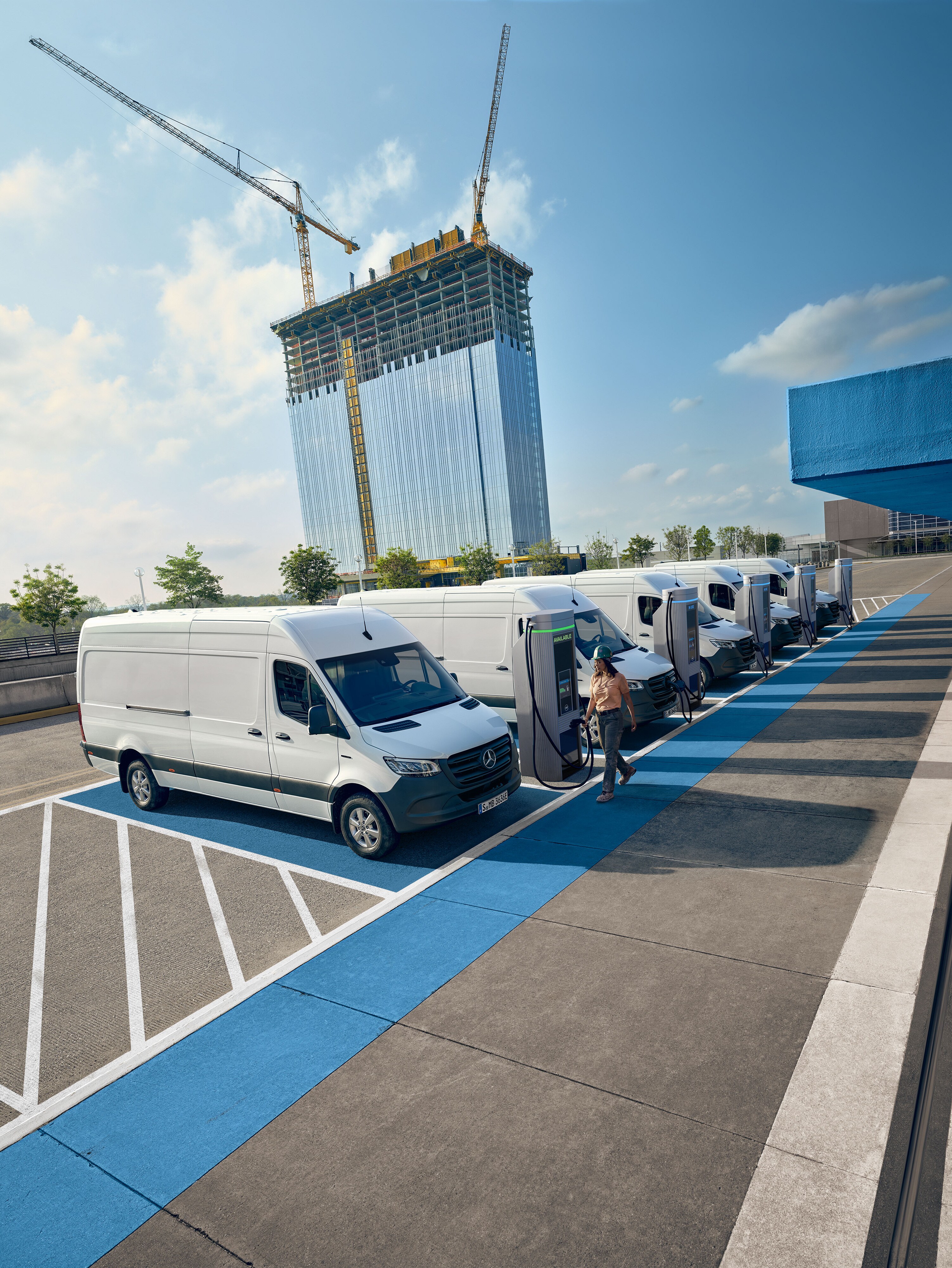 Several white Mercedes-Benz Sprinter vans charging at charging stations.