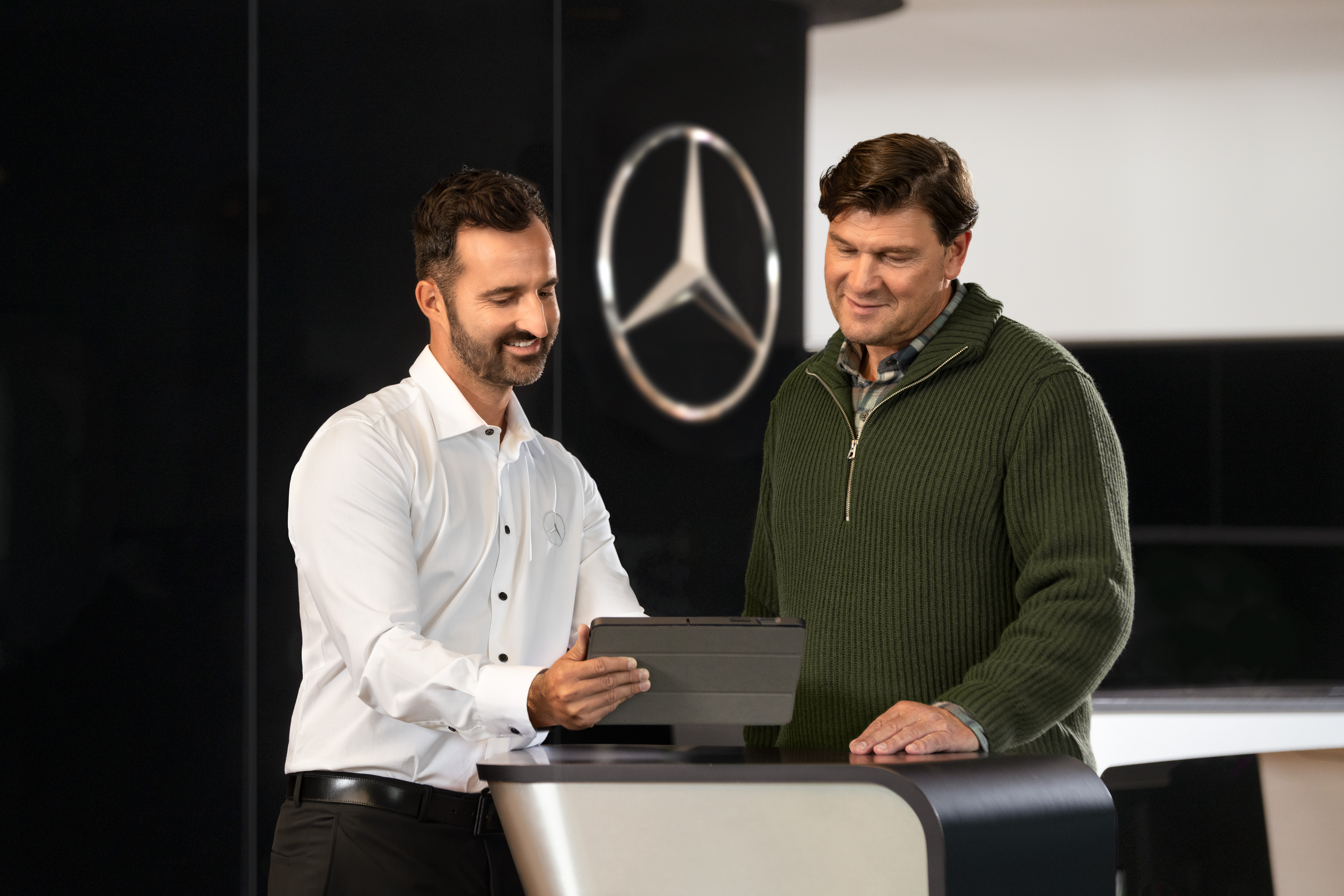Mercedes-Benz | Van Care | Individual Support Mercedes employee advises customers at the counter with a tablet – individual support and commercial advice in the dealership.