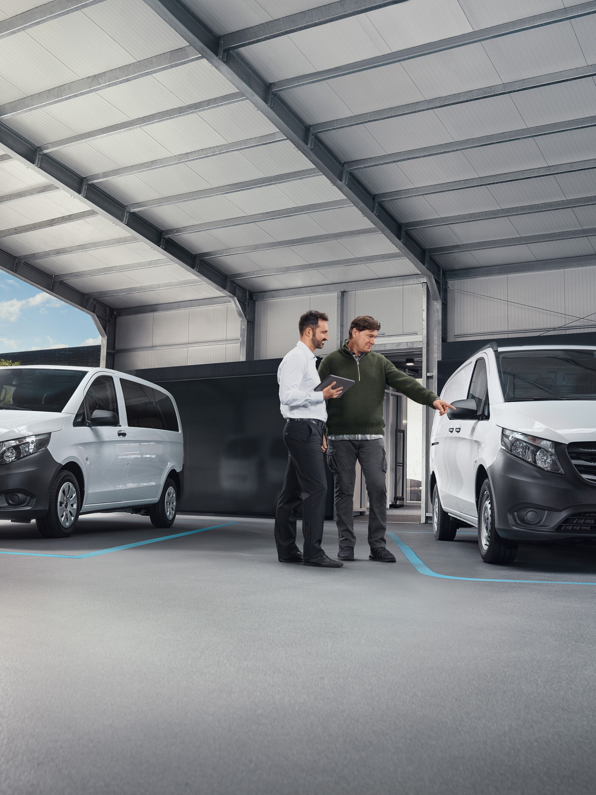 Two people talking in a worksop standing in front of two white Mercedes-Benz vans.
