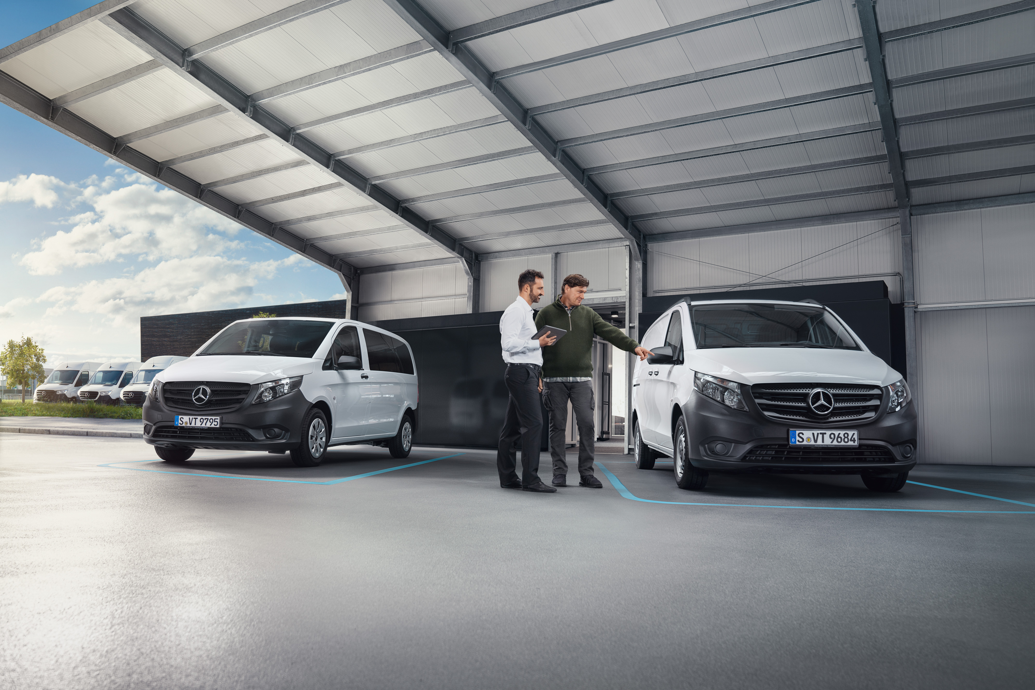 Mercedes-Benz | Convenience | Digital customer reception Two people talking in a worksop standing in front of two white Mercedes-Benz vans.