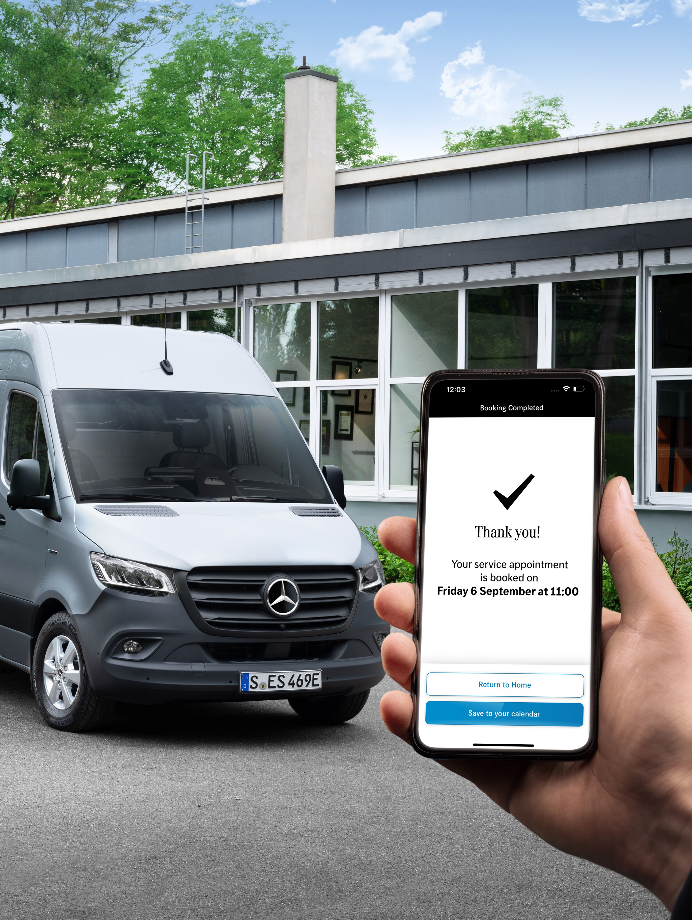 A grey Mercedes-Benz Sprinter van in front of a office with a person holding a smartphone in the foreground.