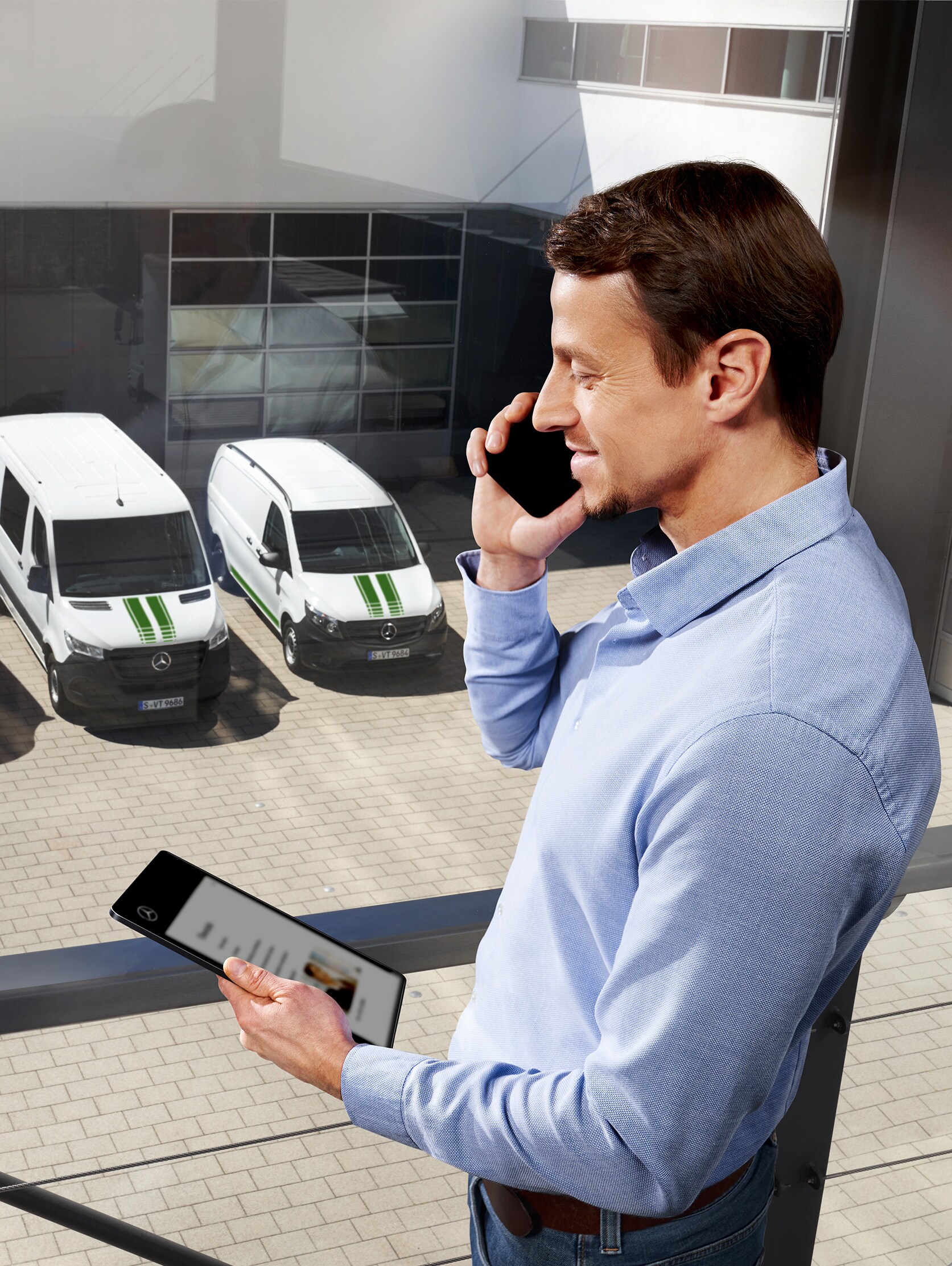 Man on the phone with tablet in front of three Mercedes-Benz vans, topic: how long is the manufacturer’s warranty at Mercedes-Benz?