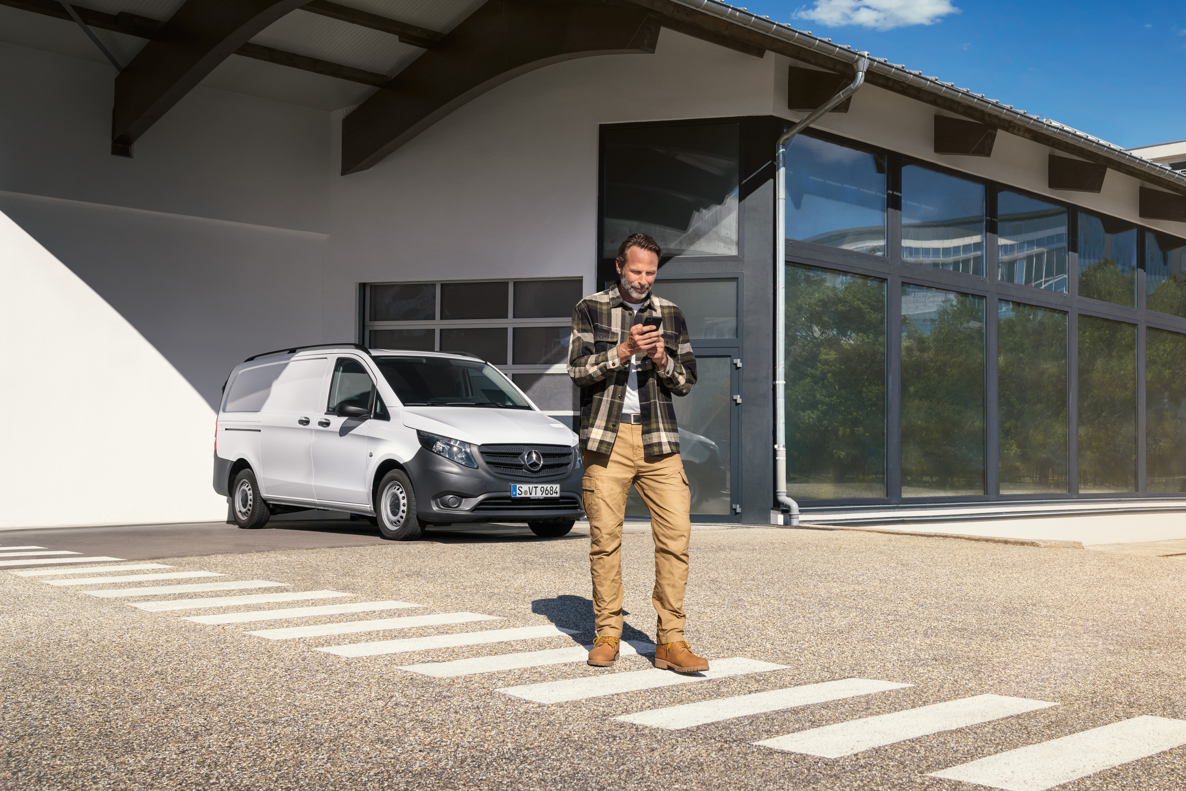 Mercedes-Benz | Electric Vehicle Service | Digital support A man standing in front of a white Mercedes-Benz Vito van using his smartphone.