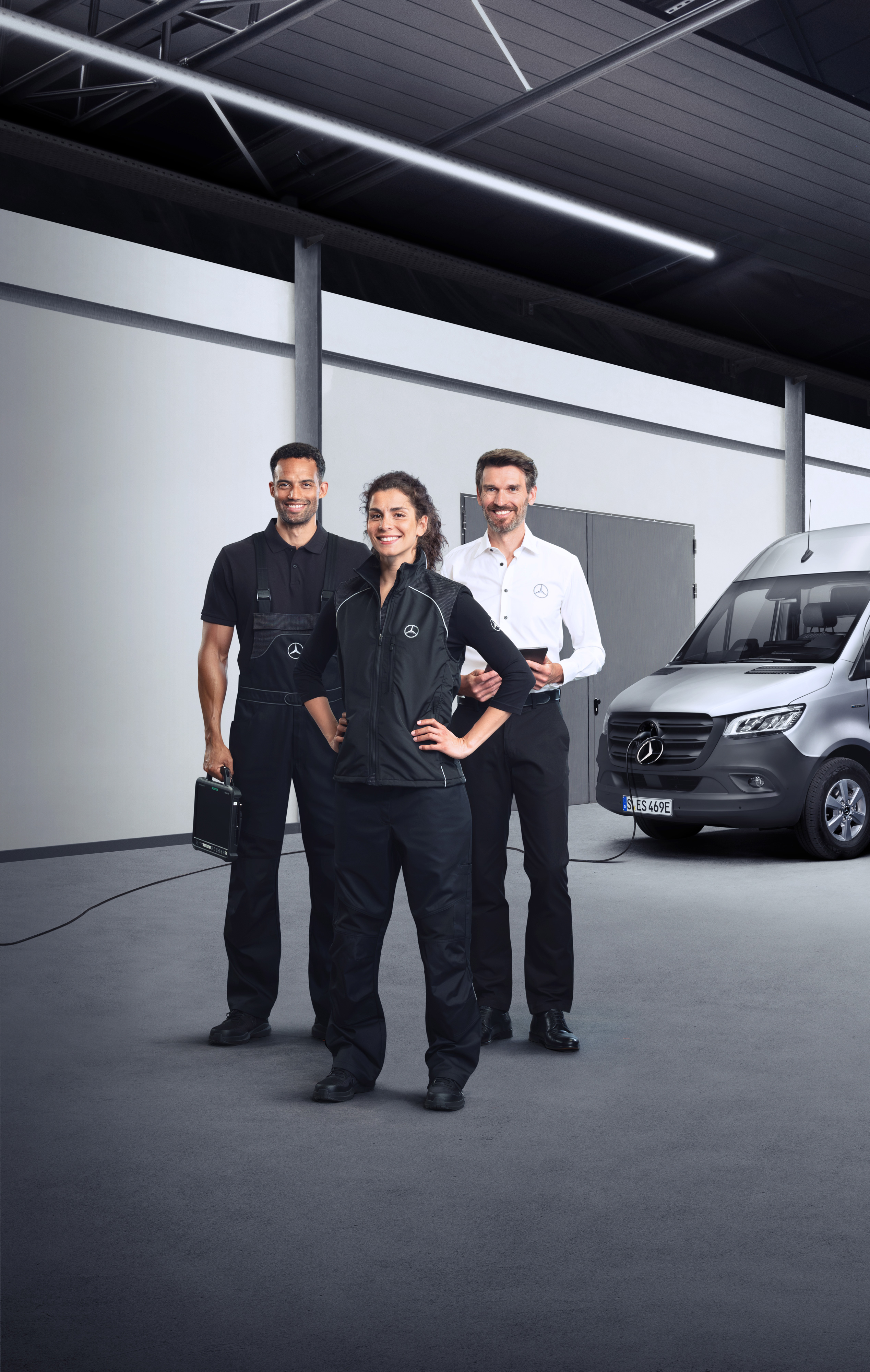Mercedes-Benz | Electric Vehicle Service Three employees in front of an electric Mercedes-Benz Sprinter van with charging cable attached.