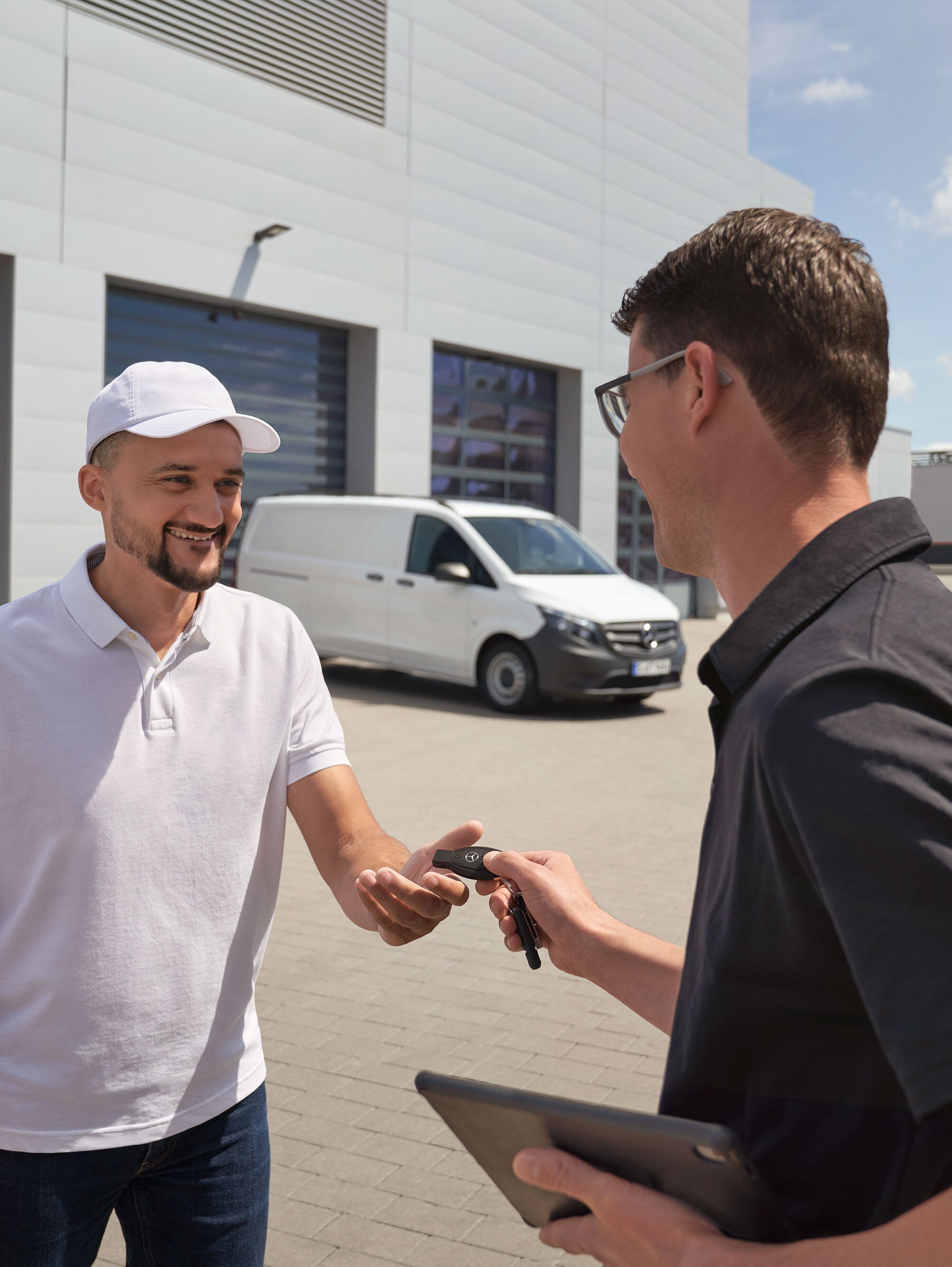Mercedes-Benz service representative handing over keys to a customer with a white Mercedes-Benz Vito van in the background.