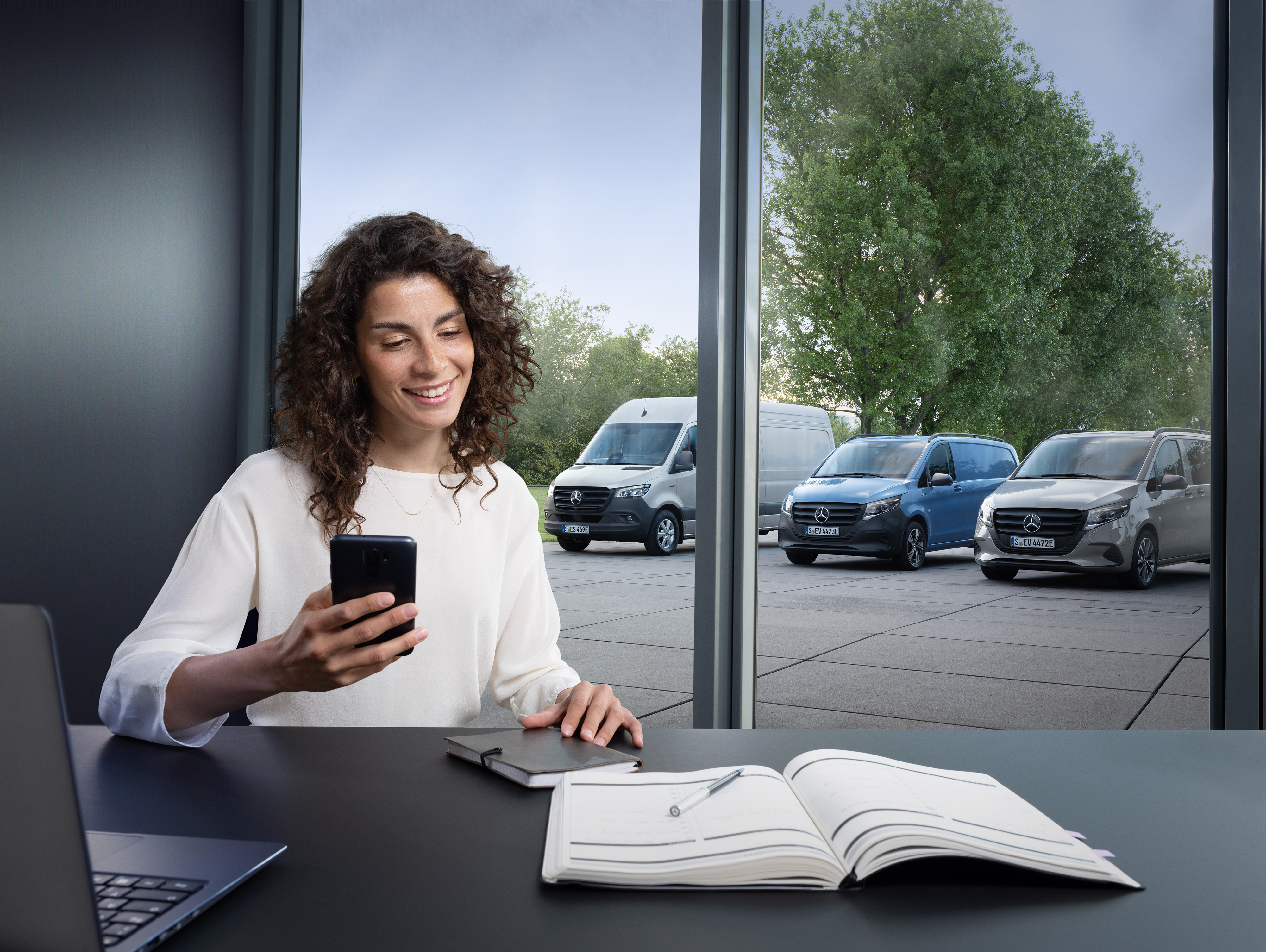 Mercedes-Benz | Van ServiceCare Woman planning on her smartphone in front of Mercedes-Benz vans