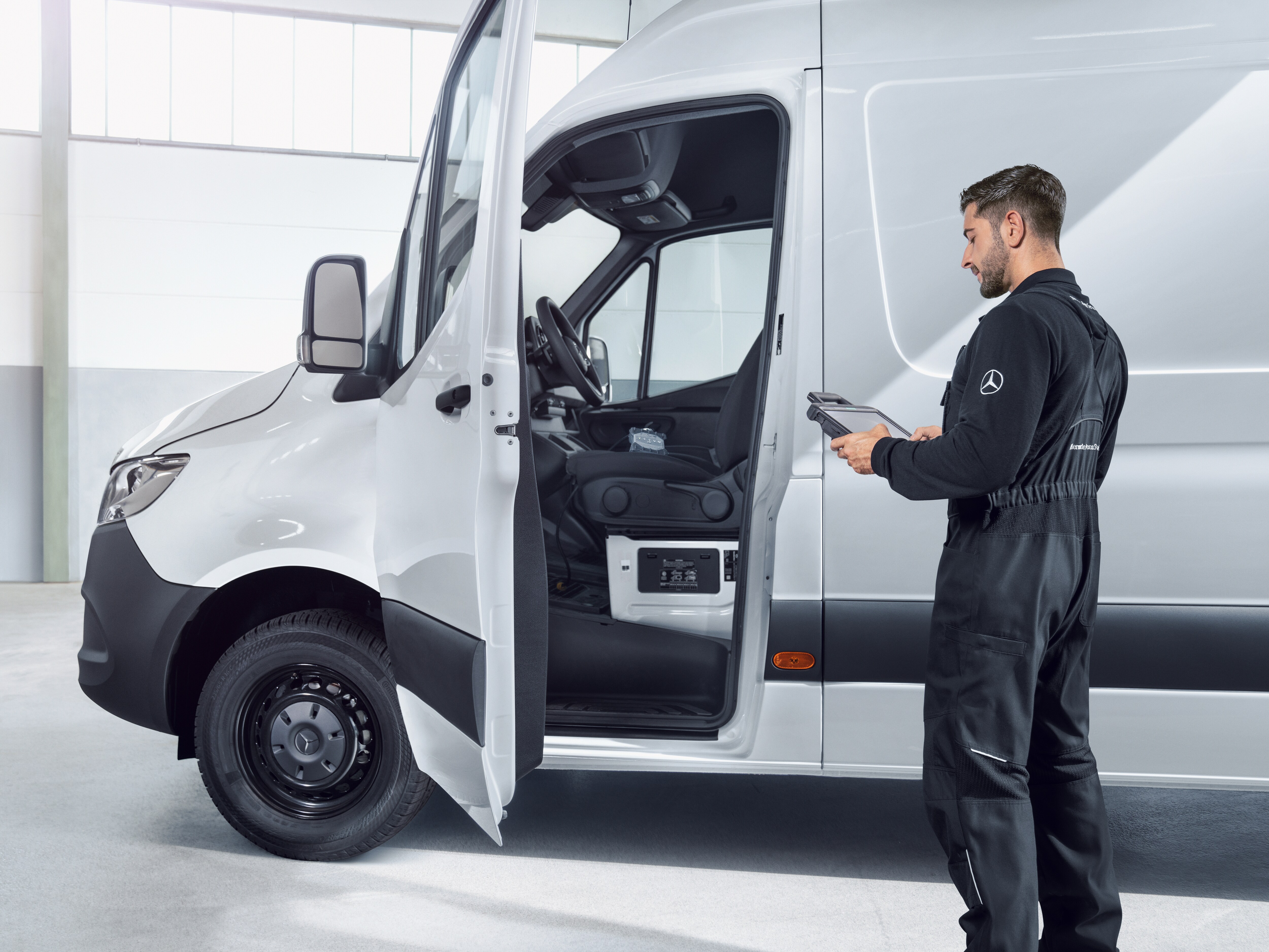 Technician in uniform inspecting a white Mercedes-Benz eSprinter van.